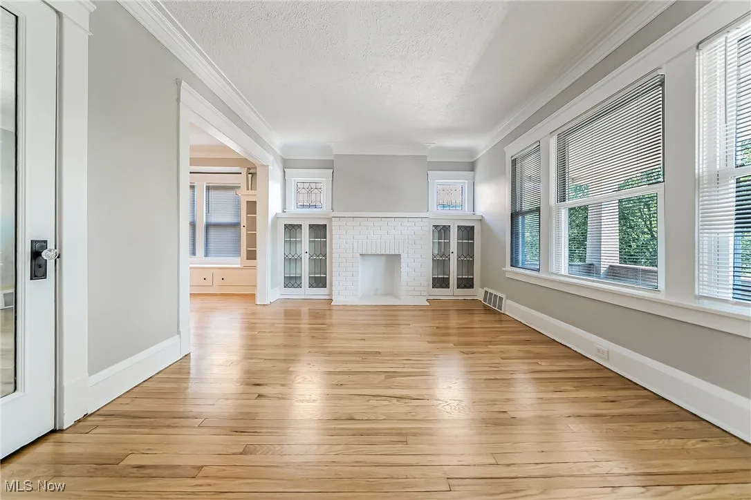 Unfurnished living room with a textured ceiling, light wood-style floors, and crown molding
