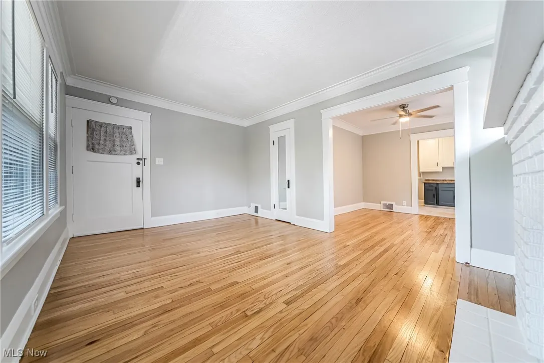 Unfurnished living room with light wood finished floors, ornamental molding, and a ceiling fan
