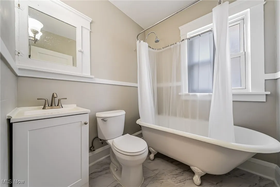 Full bath with marble look tile flooring, vanity, and shower / bath combo with shower curtain
