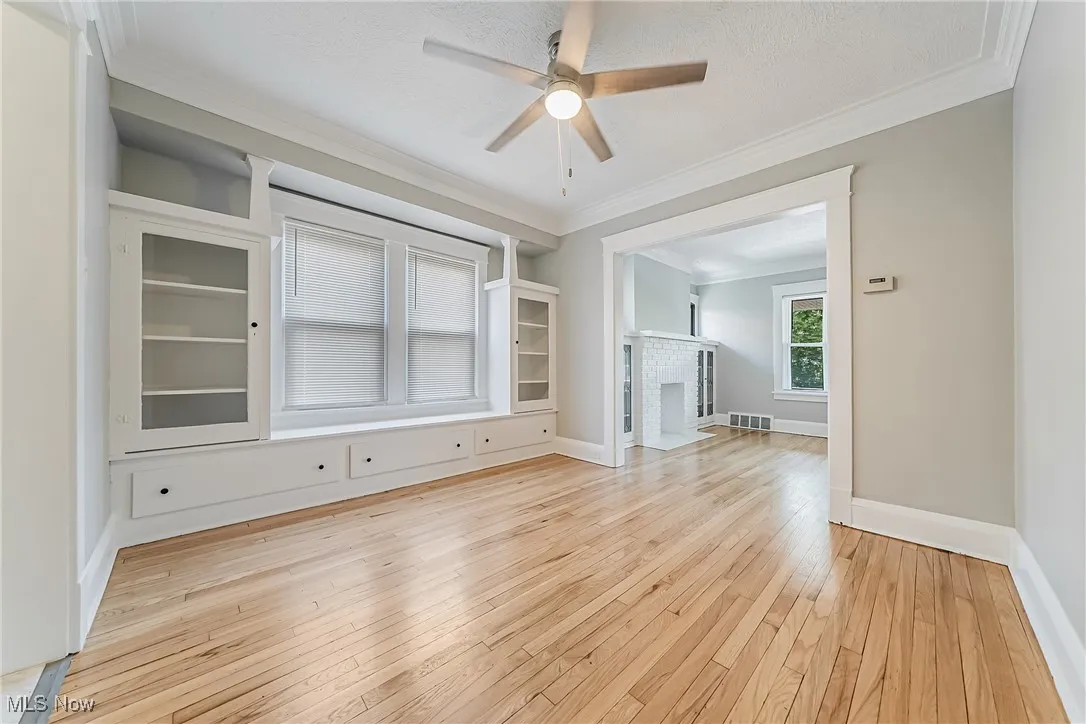 Empty room with light wood-style flooring, a ceiling fan, crown molding, and a brick fireplace