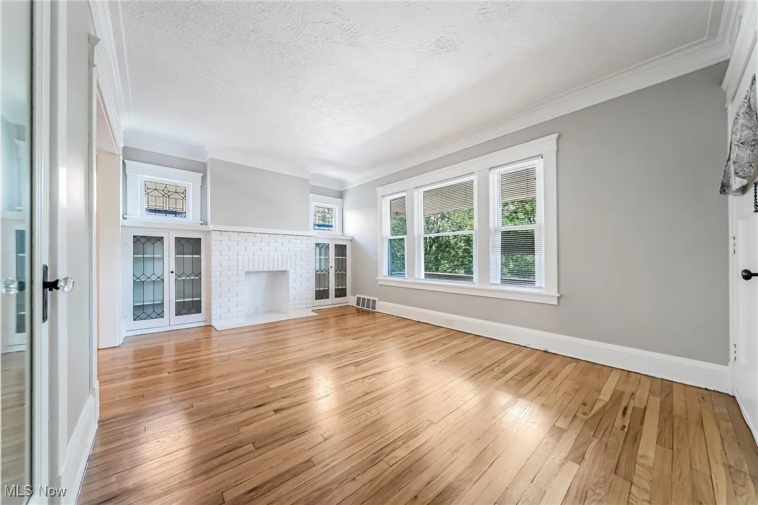 Unfurnished living room with wood-type flooring, crown molding, a brick fireplace, and a textured ceiling