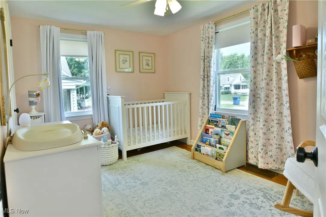 Bedroom with a crib, wood finished floors, and a ceiling fan