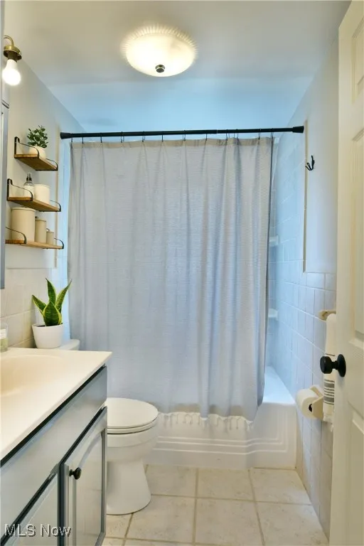 Bathroom with tile patterned flooring, vanity, shower / bath combo with shower curtain, and tile walls