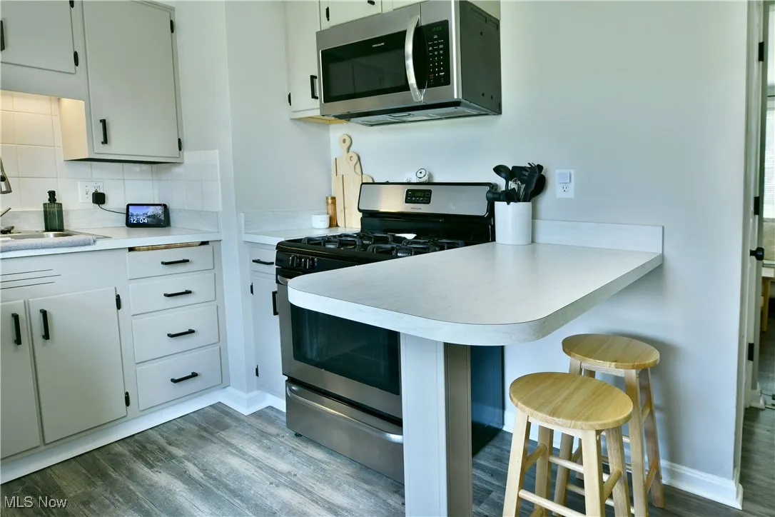 Kitchen with appliances with stainless steel finishes, dark wood-style floors, a kitchen bar, light countertops, and a peninsula