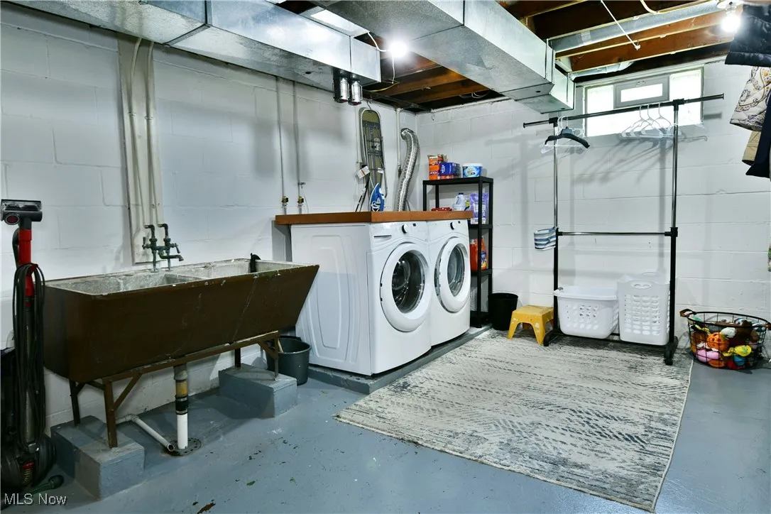 Washroom featuring washing machine and clothes dryer and concrete block wall