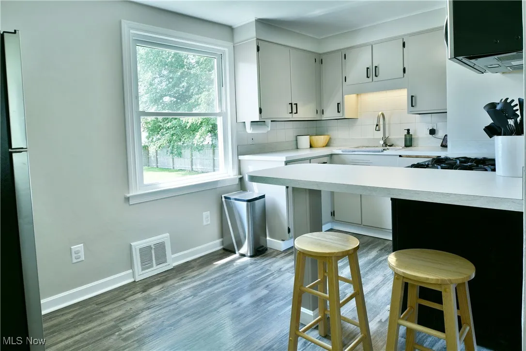 Kitchen featuring light countertops, tasteful backsplash, a breakfast bar, wood finished floors, and stovetop