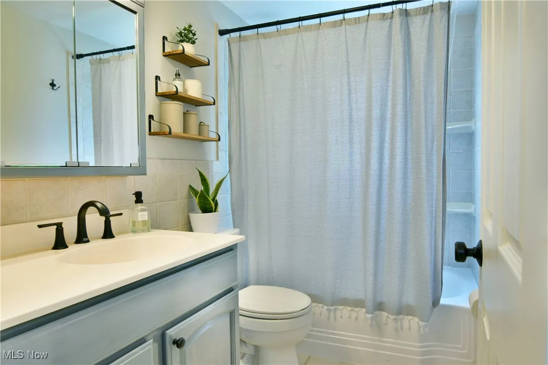 Full bathroom with vanity, shower / bath combo, tasteful backsplash, and tile walls