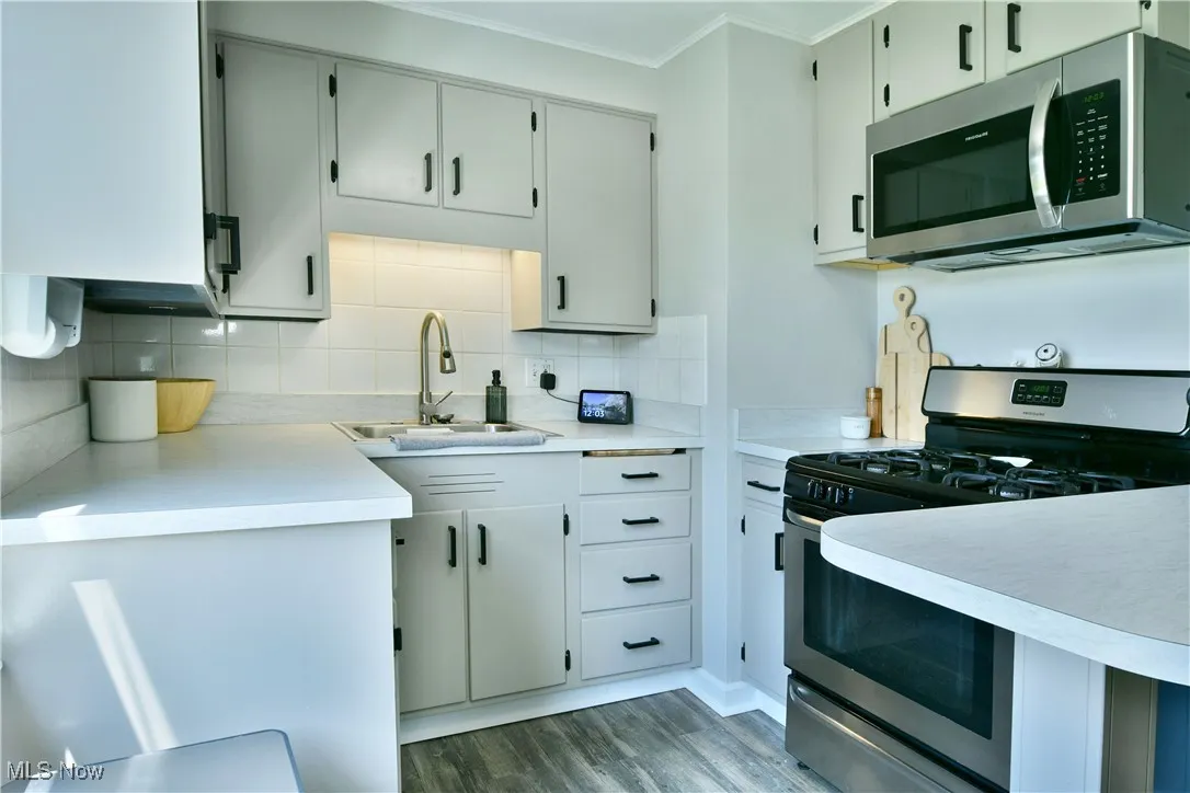 Kitchen with appliances with stainless steel finishes, ornamental molding, light countertops, tasteful backsplash, and wood finished floors