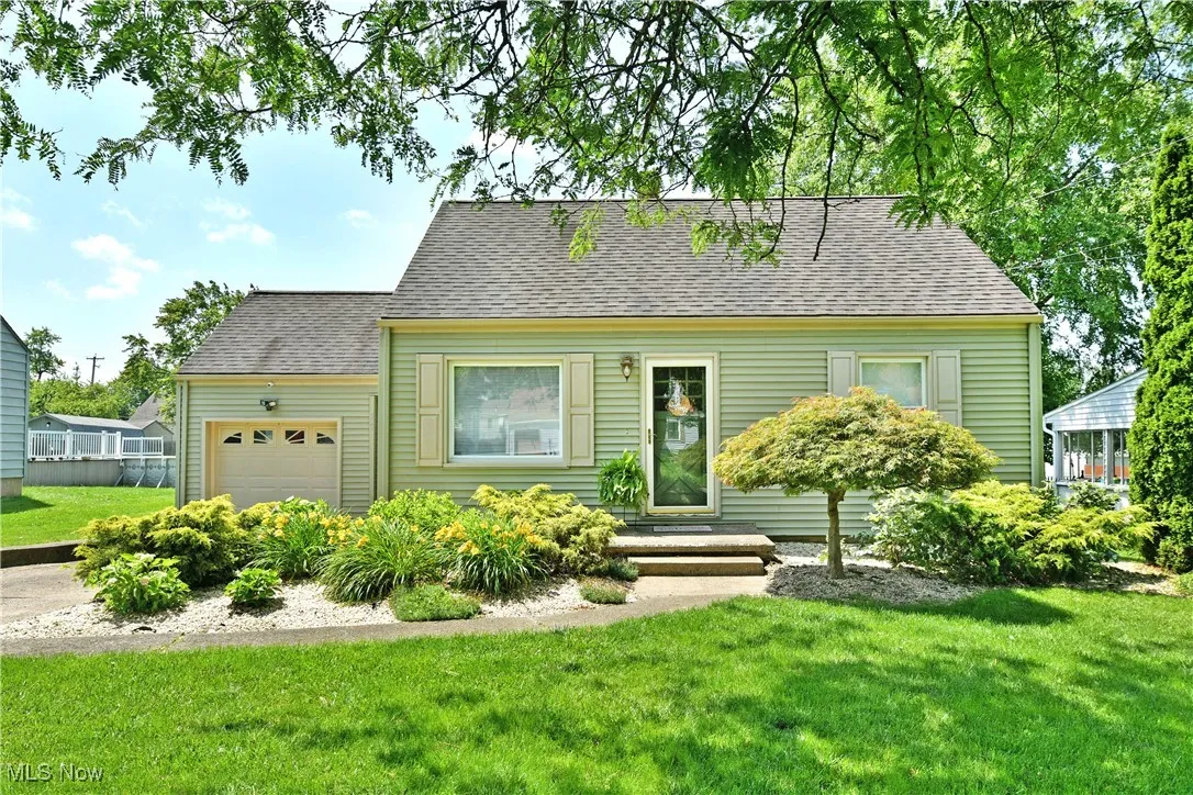 Cape cod house featuring an attached garage, a front yard, and roof with shingles