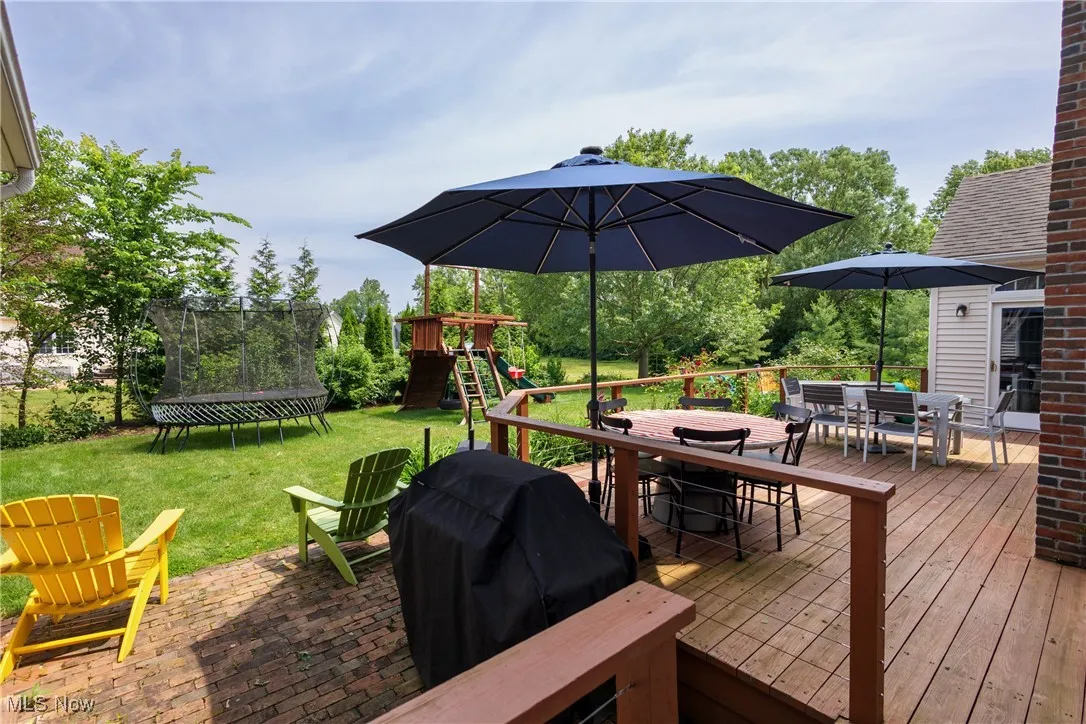 Wooden terrace with outdoor dining area, a trampoline, a playground, a yard, and area for grilling
