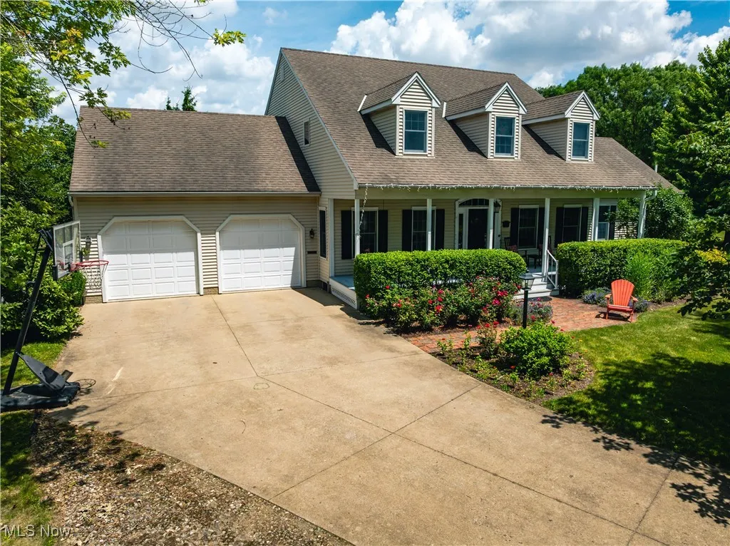 New england style home with covered porch, a garage, concrete driveway, roof with shingles, and a front yard