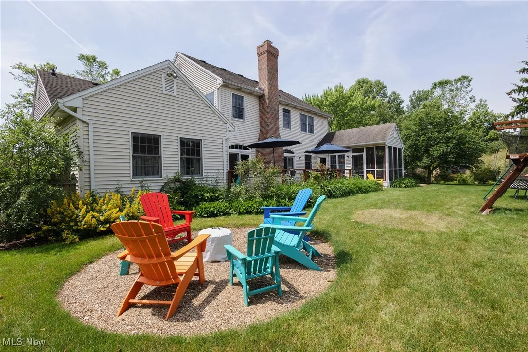 Back of property with a sunroom, an outdoor fire pit, a yard, a shingled roof, and a chimney