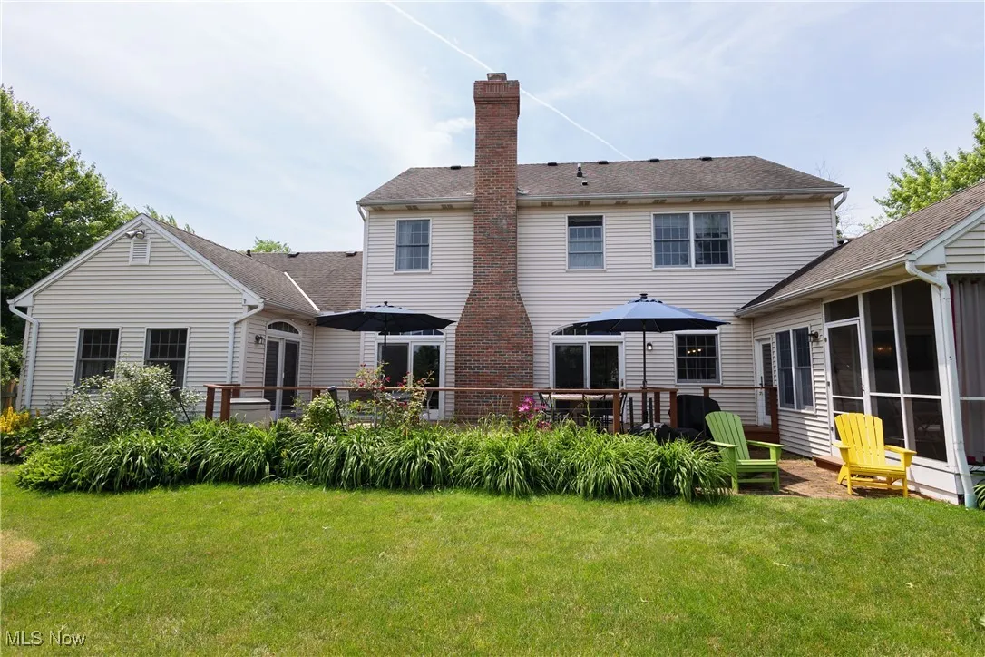 Rear view of house featuring a chimney, a lawn, a sunroom, and a wooden deck