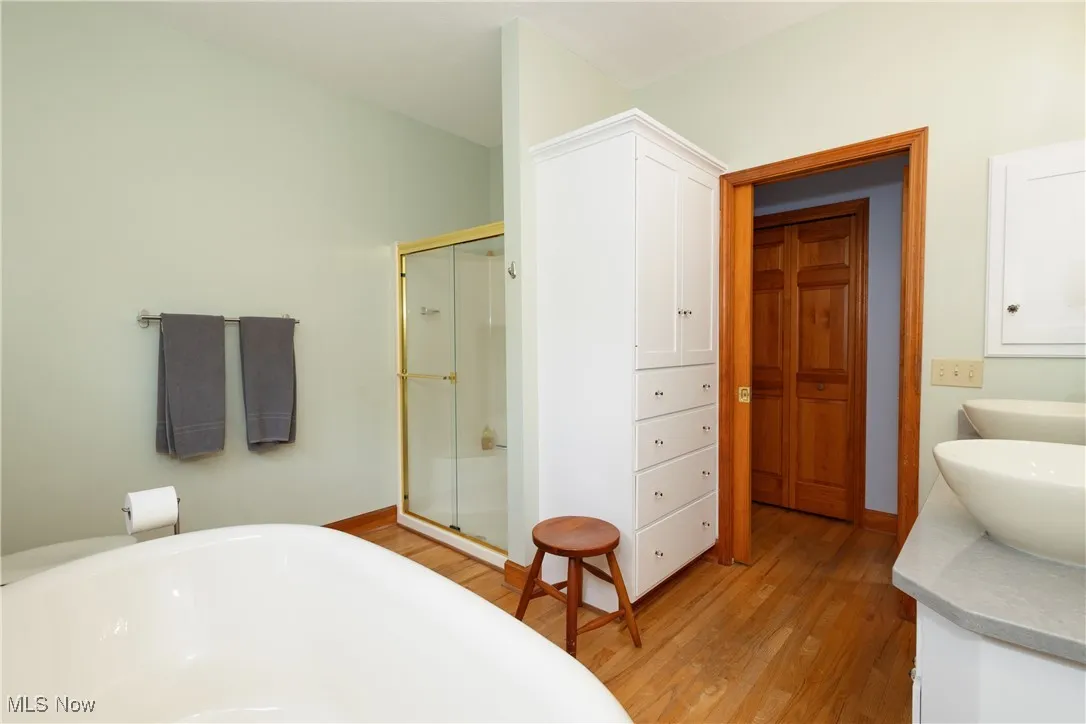 Full bath with a shower stall, double vanity, a freestanding bath, and wood finished floors