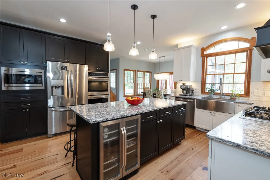Kitchen with appliances with stainless steel finishes, wine cooler, dark cabinetry, a center island, and light stone counters