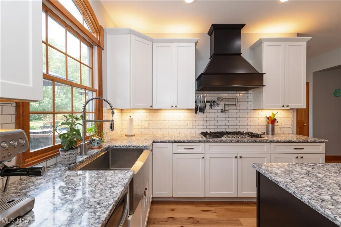 Kitchen with wall chimney range hood, white cabinets, and recessed lighting