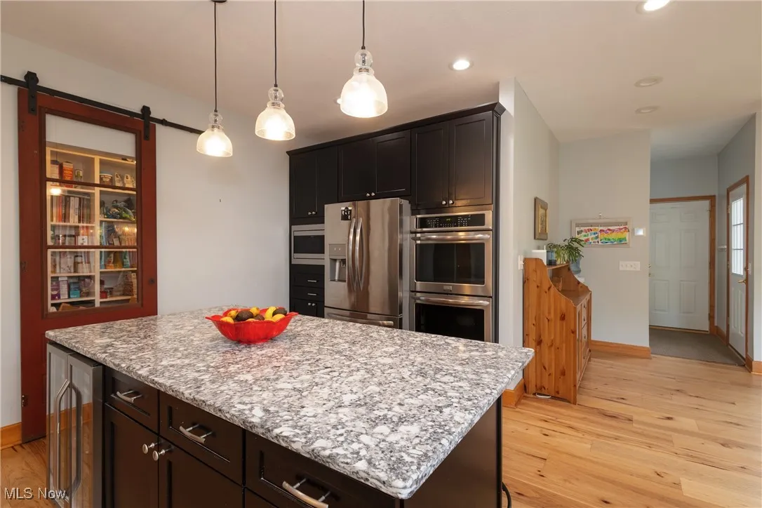 Kitchen featuring stainless steel appliances, light wood-type flooring, wine cooler, a kitchen island, and decorative light fixtures
