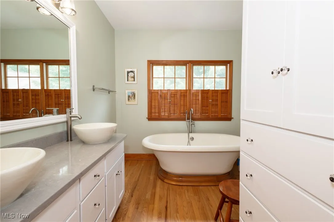 Full bath with wood finished floors, double vanity, and a soaking tub