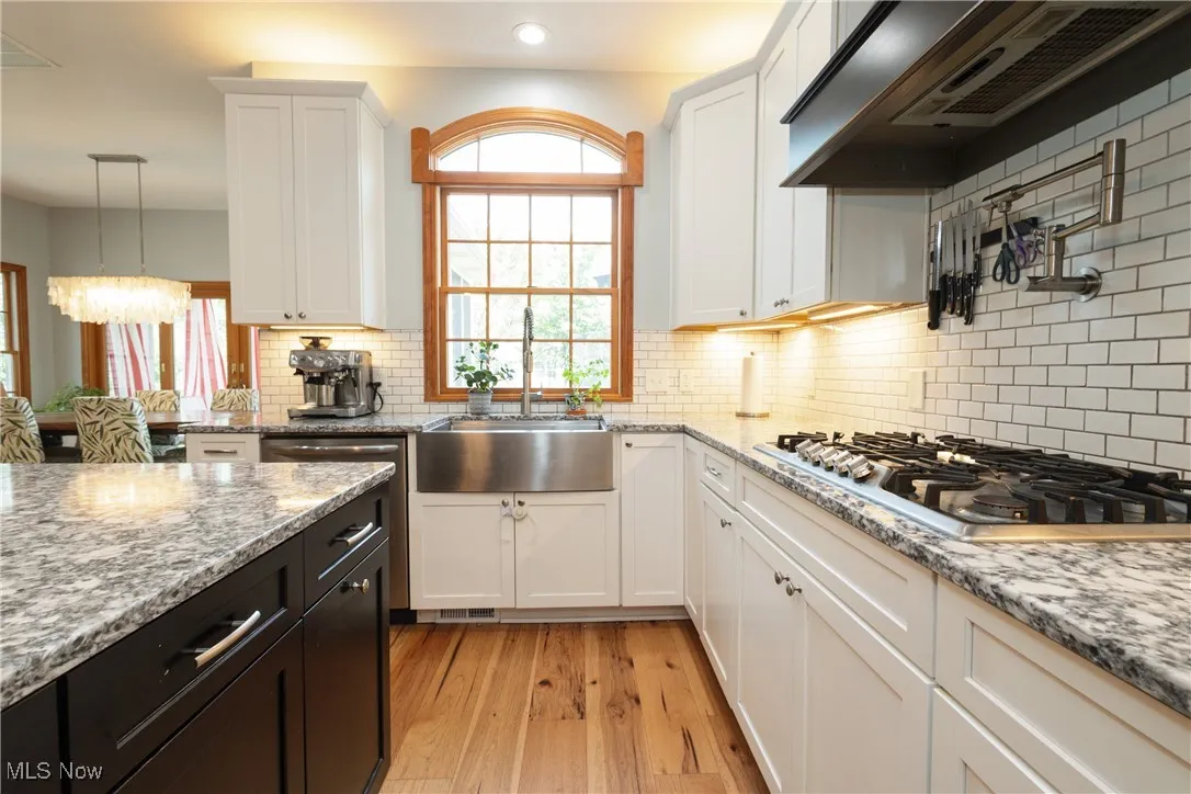 Kitchen with stainless steel gas stovetop, exhaust hood, white cabinets, light wood-style flooring, and decorative backsplash