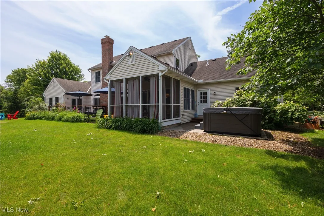 Rear view of property featuring a hot tub, a sunroom, a yard, a patio, and roof with shingles