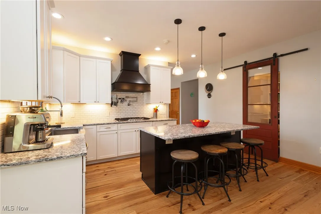 Kitchen featuring custom exhaust hood, white cabinetry, a kitchen island, light wood finished floors, and decorative backsplash