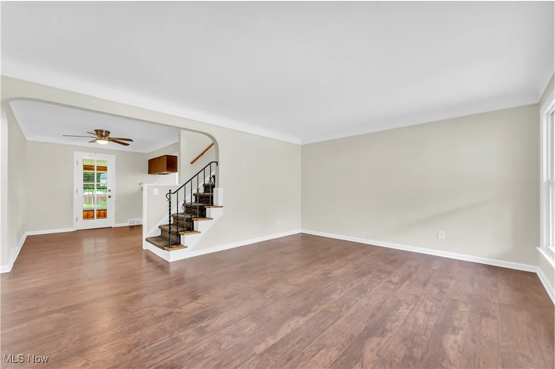 Spare room with stairs, dark wood-type flooring, a ceiling fan, and arched walkways