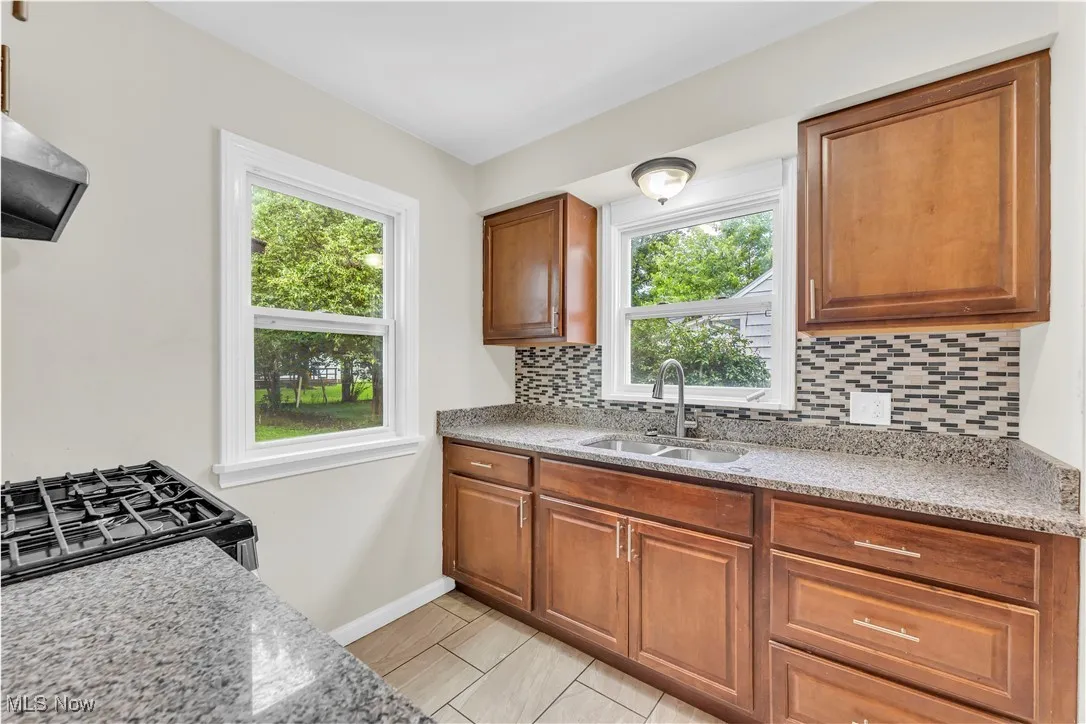 Kitchen featuring tasteful backsplash, range with gas cooktop, brown cabinets, light stone counters, and ventilation hood