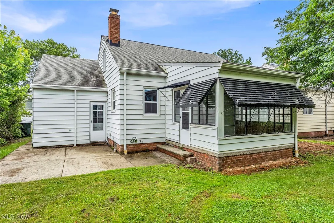 Rear view of house with a sunroom, a chimney, a yard, and a shingled roof