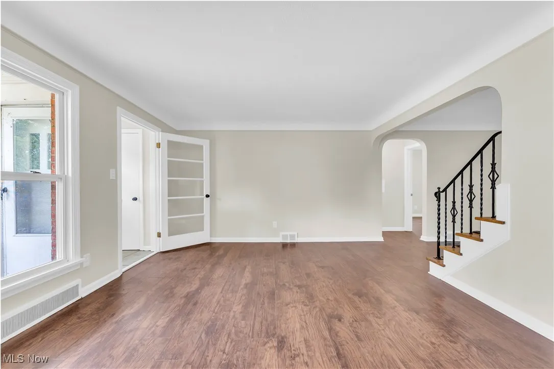 Unfurnished room with arched walkways, wood finished floors, plenty of natural light, and stairway