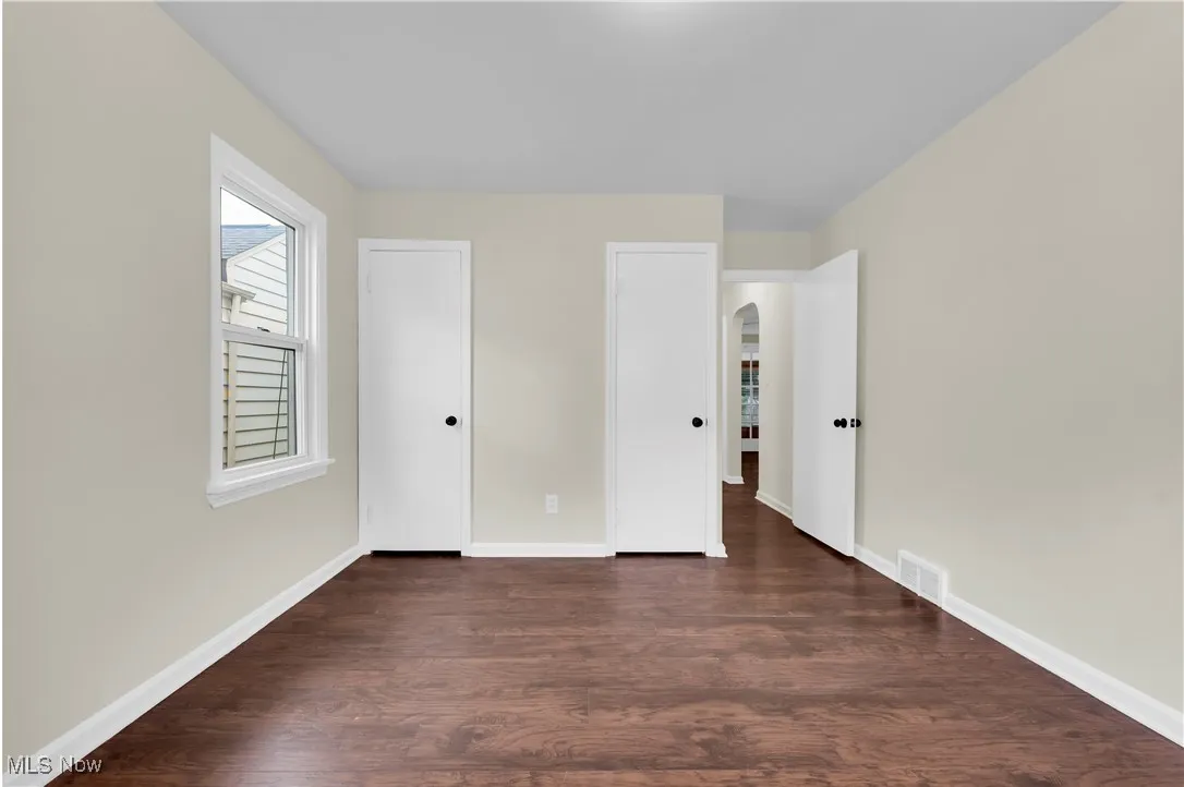 Unfurnished bedroom featuring arched walkways and dark wood-style flooring