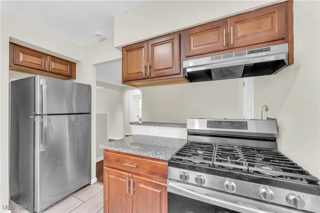 Kitchen featuring stainless steel appliances, under cabinet range hood, brown cabinetry, and arched walkways