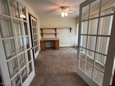 Unfurnished office with french doors, dark carpet, and ceiling fan