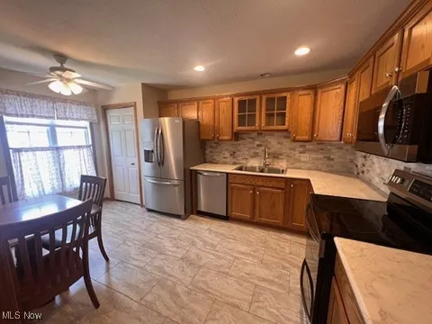 Kitchen featuring stainless steel appliances, brown cabinetry, light countertops, backsplash, and ceiling fan