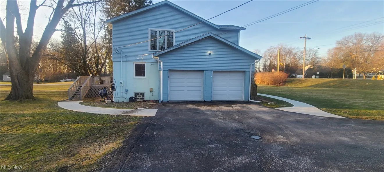 View of home's exterior featuring driveway,  front & back yard areas, an attached garage, & deck