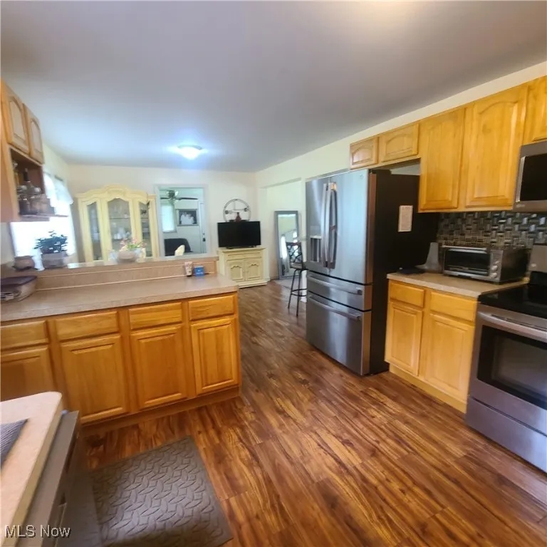 Kitchen with stainless steel appliances, wood finished floors, light countertops, a peninsula, and tasteful backsplash