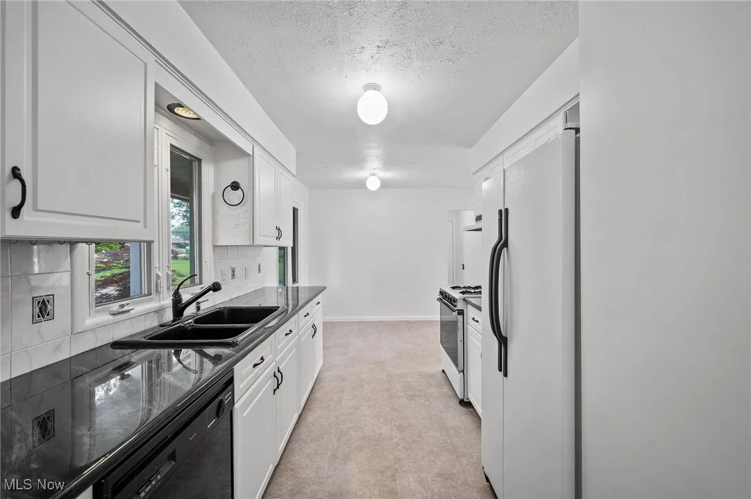 Kitchen with white appliances, white cabinets, a textured ceiling, decorative backsplash, and light carpet