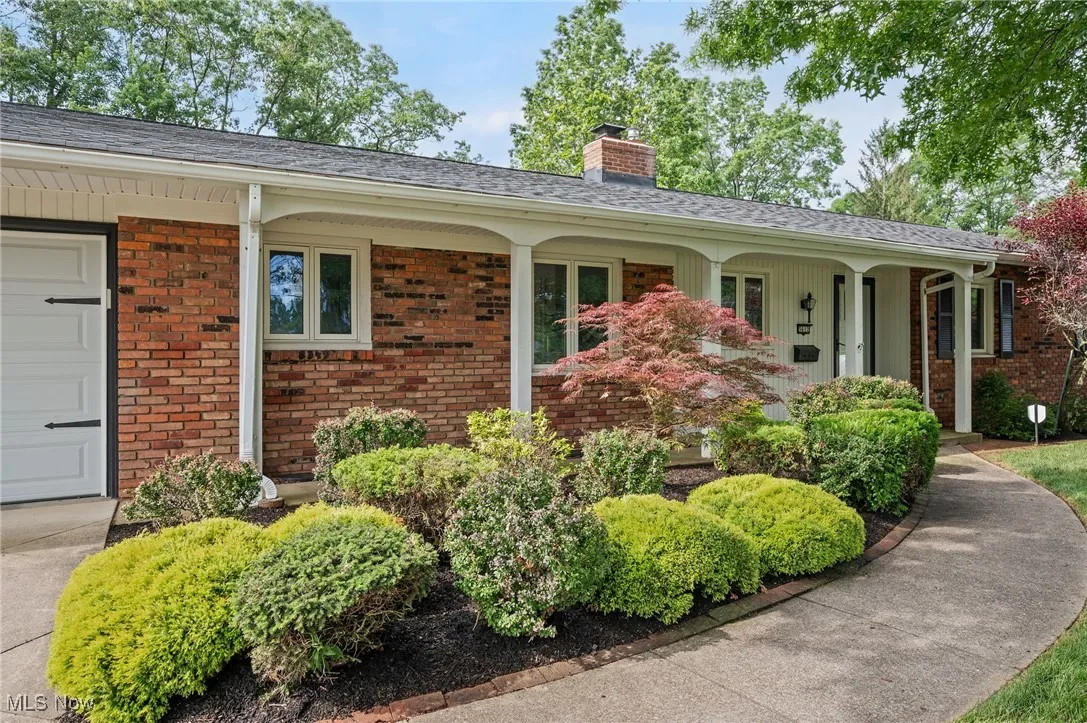 View of front of house with a chimney, a porch, brick siding, and a garage