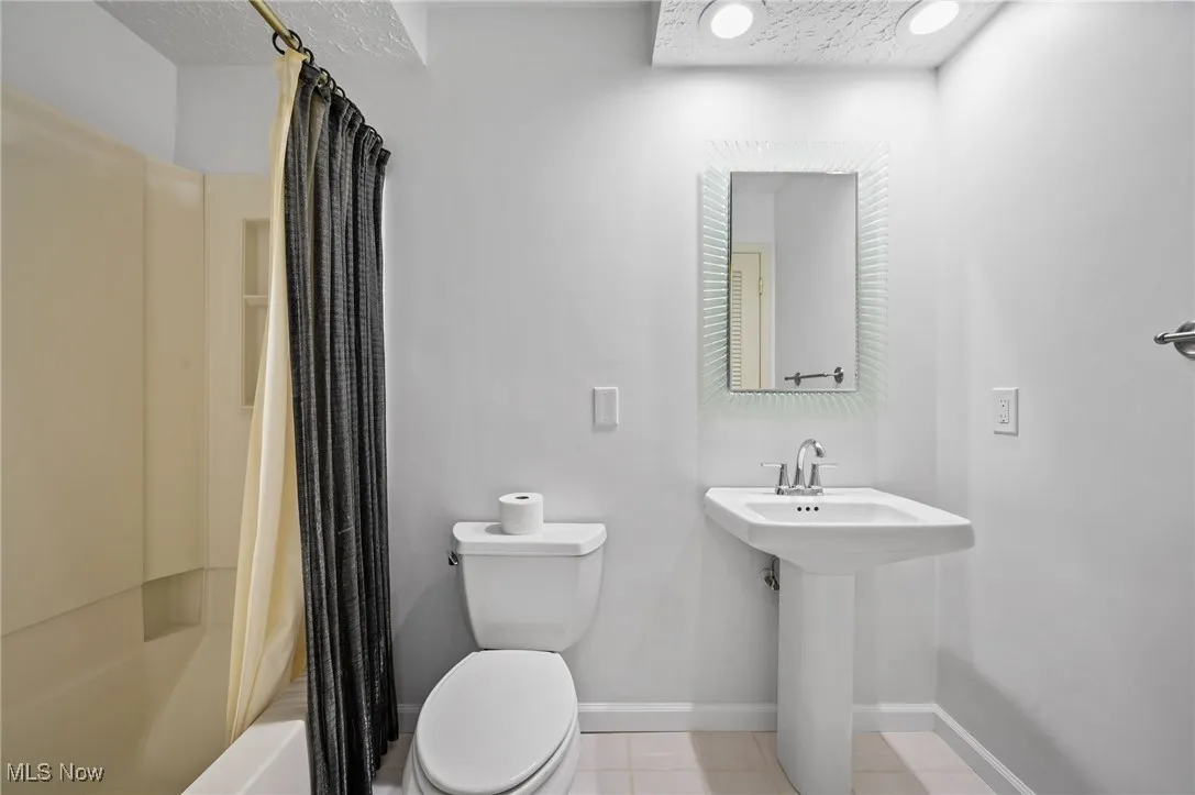 Full bathroom featuring shower / bath combo with shower curtain, tile patterned floors, and a textured ceiling