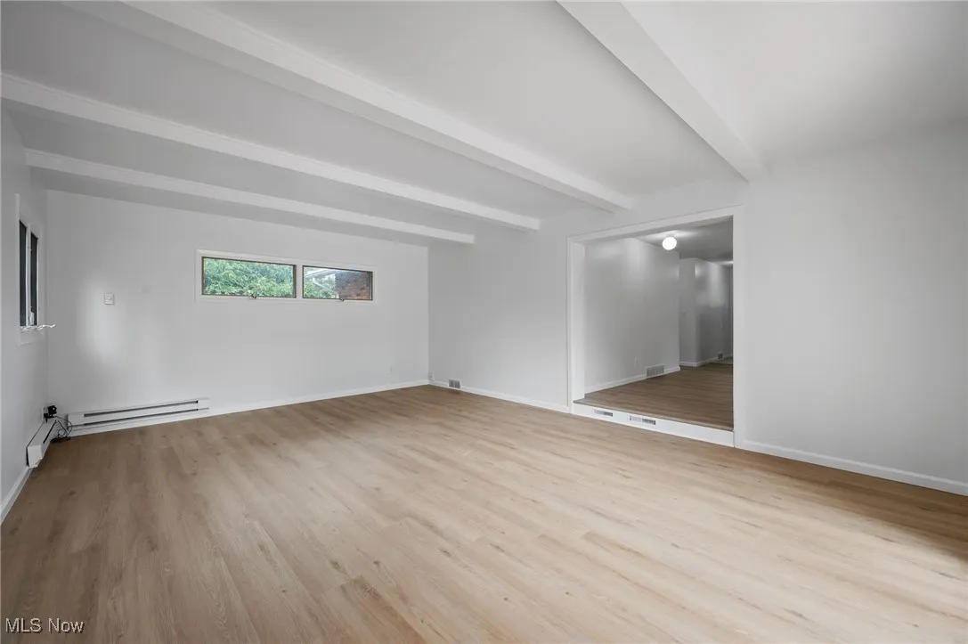 Empty room with a baseboard radiator, beam ceiling, and wood finished floors