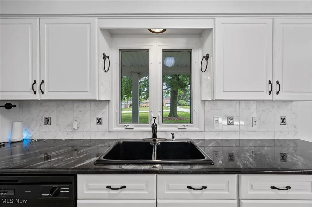 Kitchen featuring black dishwasher, white cabinets, backsplash, and dark stone counters