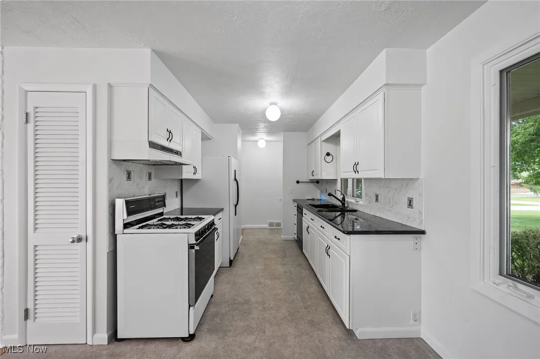 Kitchen with white appliances, under cabinet range hood, decorative backsplash, white cabinetry, and a textured ceiling