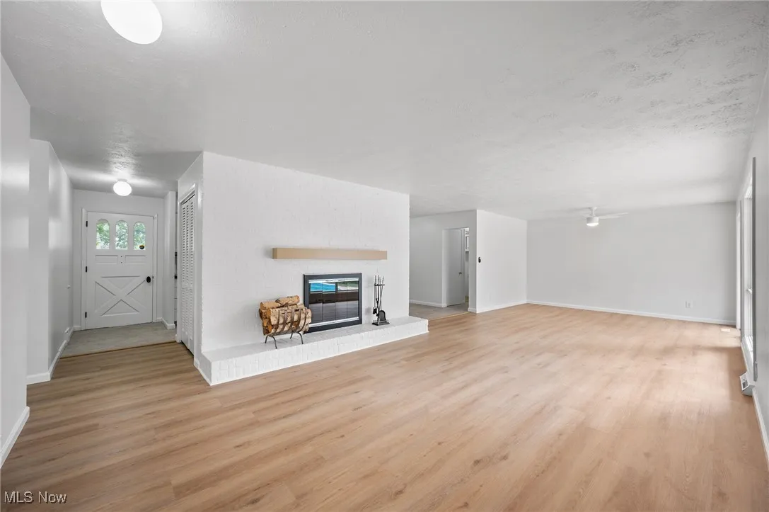 Unfurnished living room with light wood finished floors, a brick fireplace, and a textured ceiling