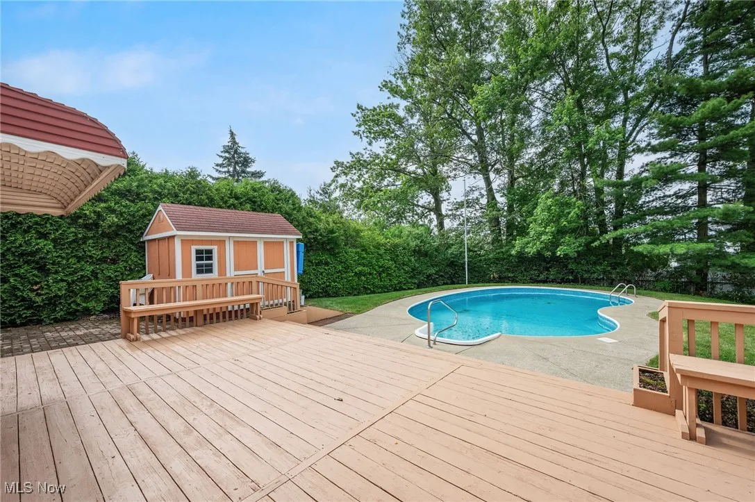 Swimming pool featuring a wooden deck, an outdoor structure, and view of wooded area