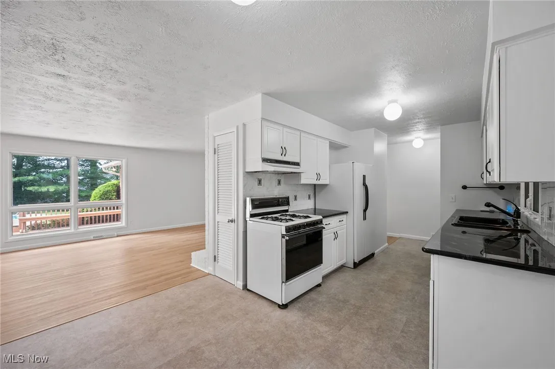 Kitchen with white range with gas cooktop, dark countertops, a textured ceiling, white cabinets, and light colored carpet