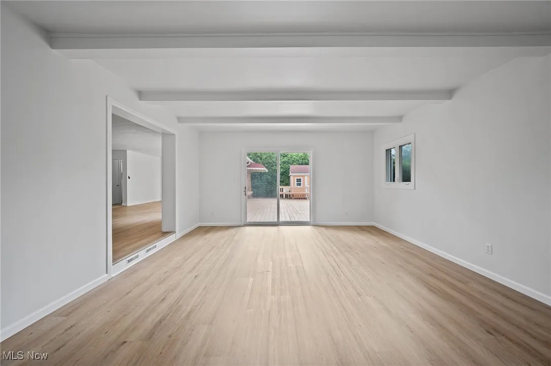 Unfurnished room with wood finished floors and beam ceiling
