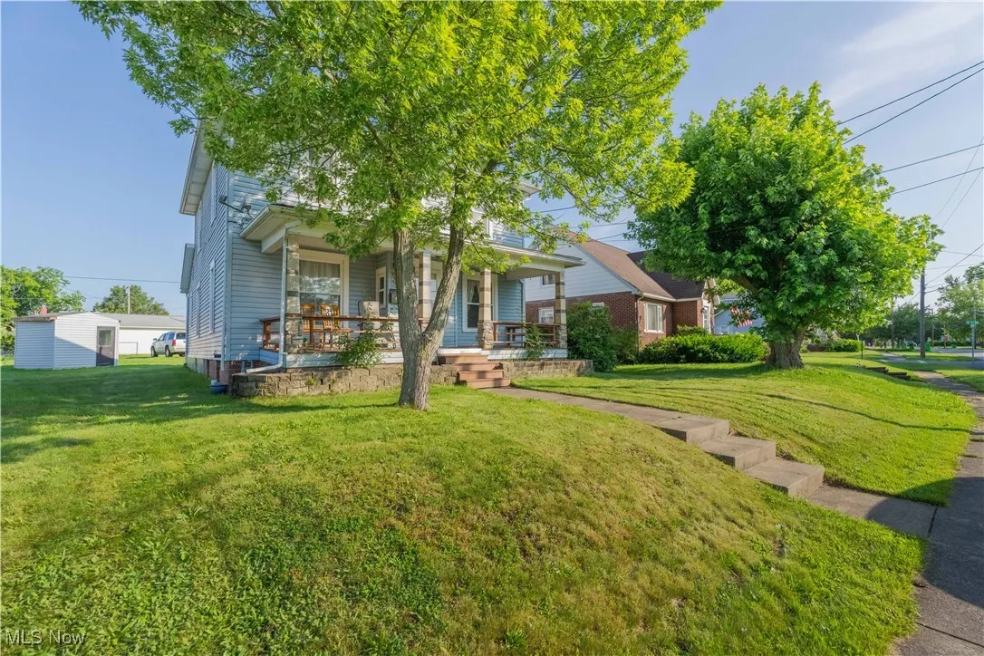 View of property hidden behind natural elements with a porch and a front lawn