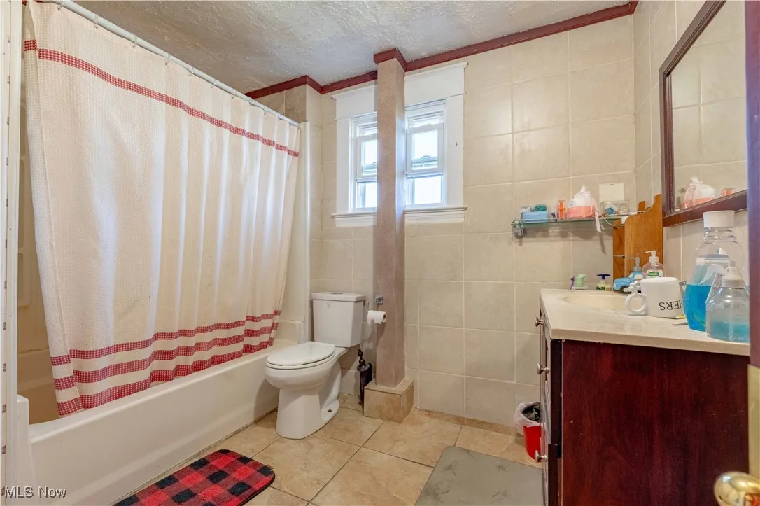 Bathroom featuring tile walls, vanity, tile patterned floors, shower / tub combo, and crown molding