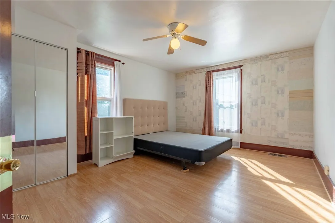 Bedroom with wood finished floors, wallpapered walls, ceiling fan, and a closet