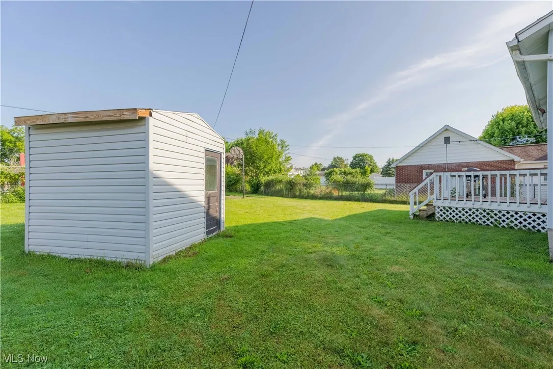 View of grassy yard with a wooden deck and a storage unit