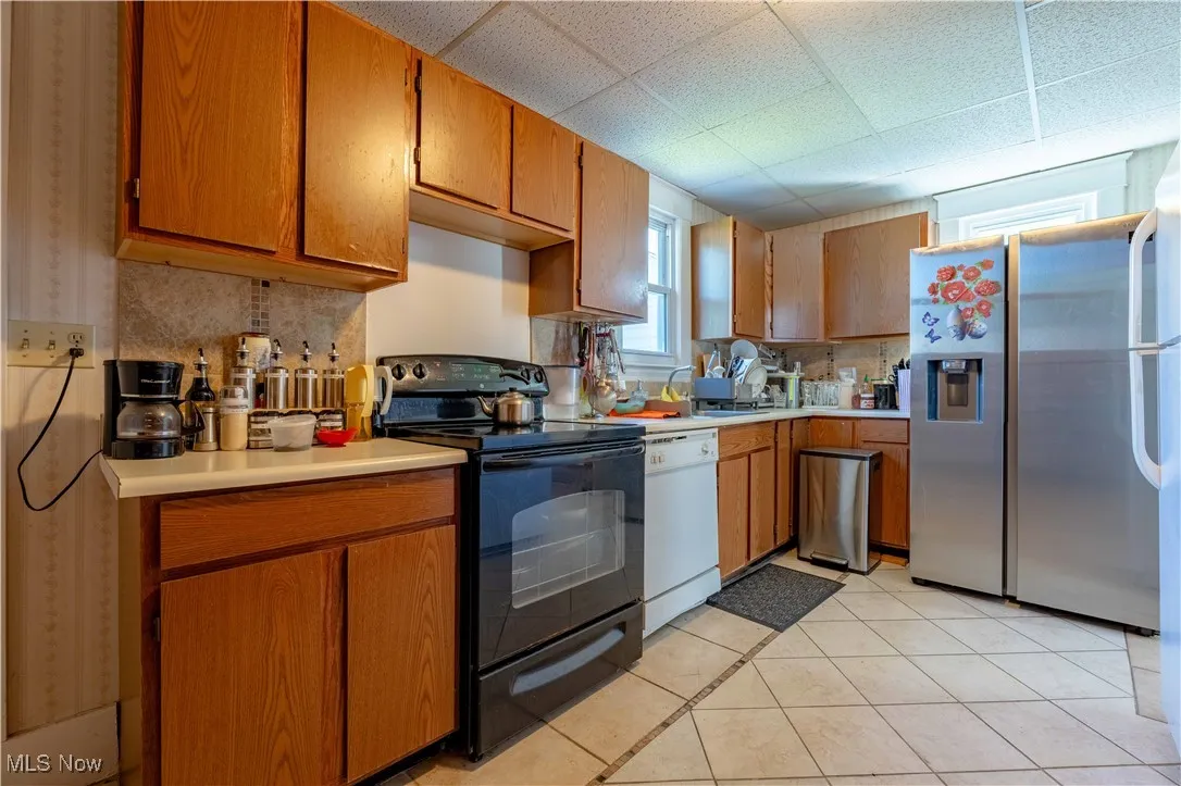 Kitchen with black range with electric cooktop, white dishwasher, light countertops, decorative backsplash, and brown cabinetry